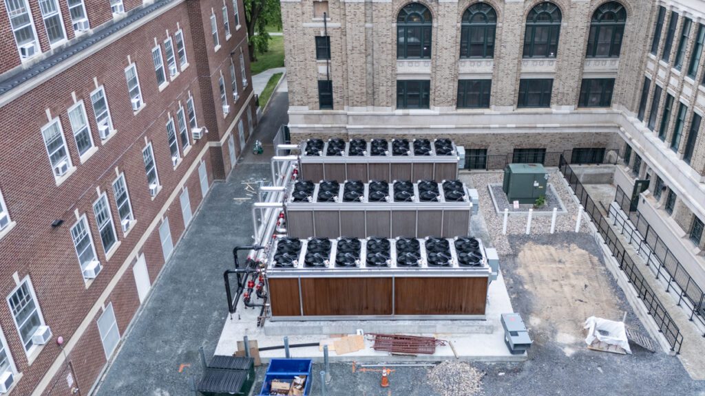 Aerial view of three rooftop HVAC units between two multi-story brick buildings, with gravel and construction materials nearby—a scene that highlights the practical application of Building Information Modeling in modern construction environments.