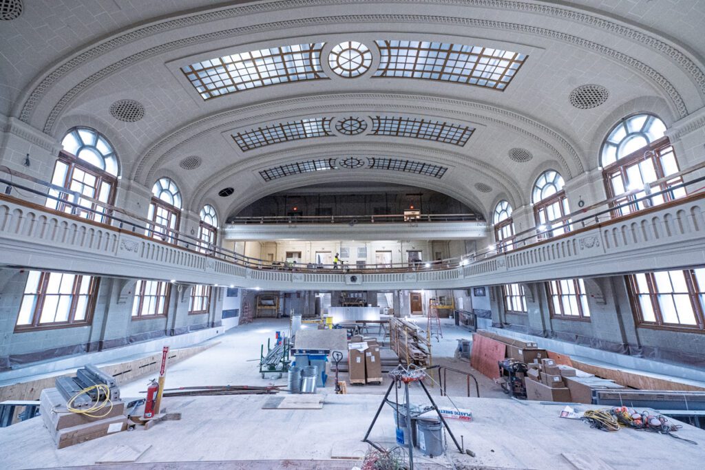 A spacious, historic hall with arched windows and a curved, detailed ceiling is under renovation, filled with construction materials, tools, and scaffolding—a process enhanced by Building Information Modeling to ensure precise restoration.