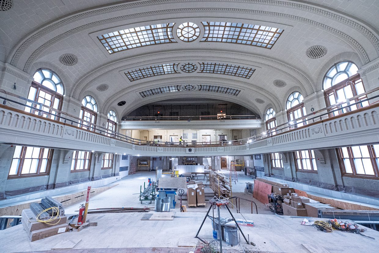 A spacious, historic hall with arched windows and a curved, detailed ceiling is under renovation, filled with construction materials, tools, and scaffolding—a process enhanced by Building Information Modeling to ensure precise restoration.