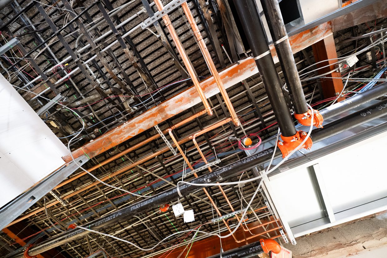 Exposed building ceiling showing electrical wires, pipes, and metal beams in a construction or renovation site.