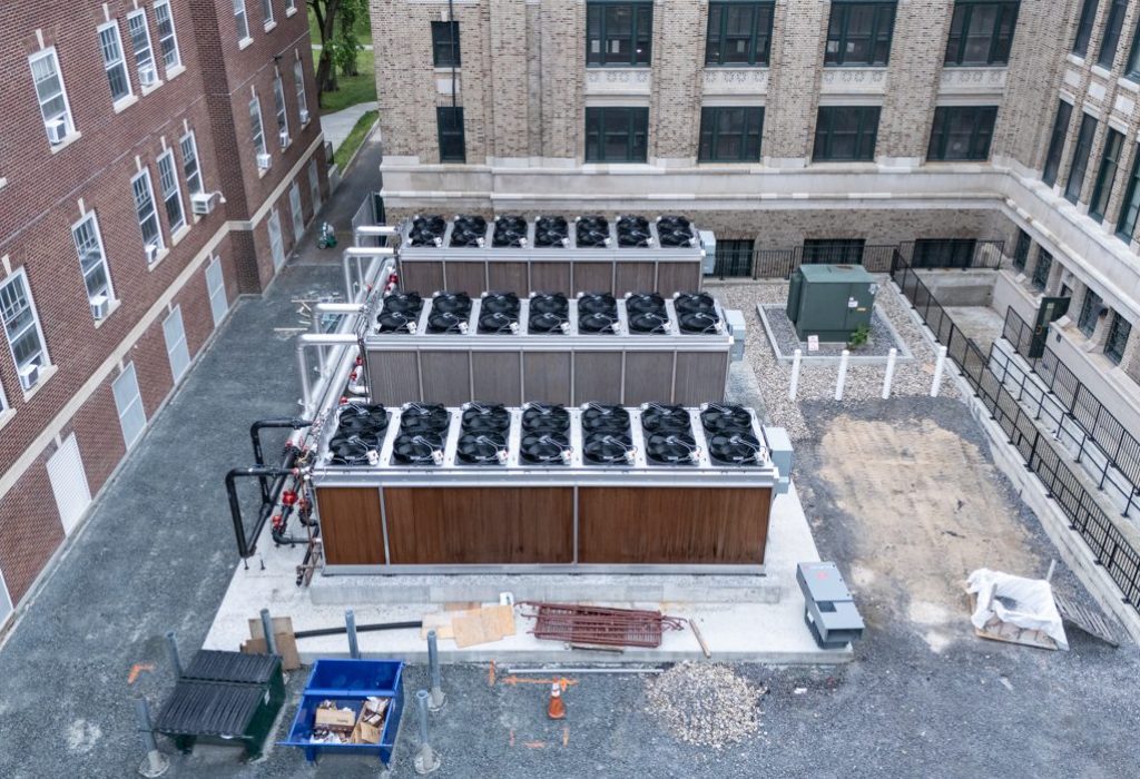 Aerial view of large industrial HVAC units next to a brick building, surrounded by gravel, construction materials, and nearby windows and doors—an ideal setting to implement Building Information Modeling for optimized facility management.