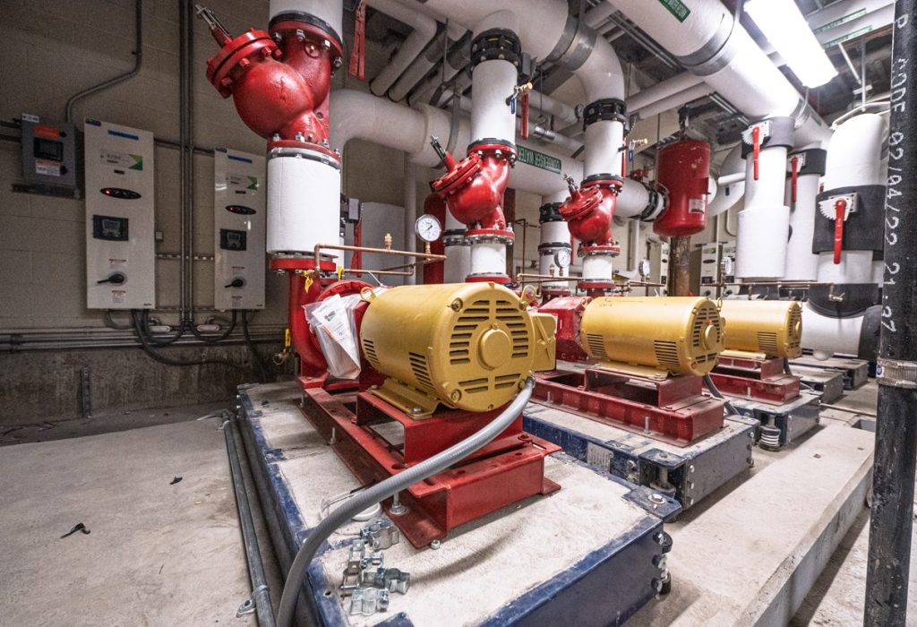 Two large yellow industrial pumps mounted on red bases, surrounded by white pipes, gauges, and control panels in a mechanical or utility room designed using Building Information Modeling.