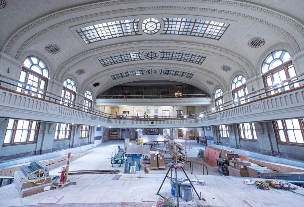 A spacious, historic hall with arched windows and a curved, detailed ceiling is under renovation, filled with construction materials, tools, and scaffolding—a process enhanced by Building Information Modeling to ensure precise restoration.